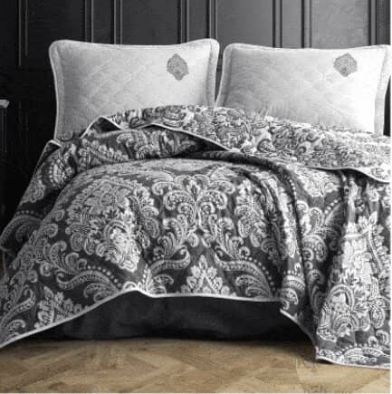 Colcha Sibiles en colores blanco y negro con dos cojines blancos sobre cama de matrimonio con fondo negro y suelo de parqué